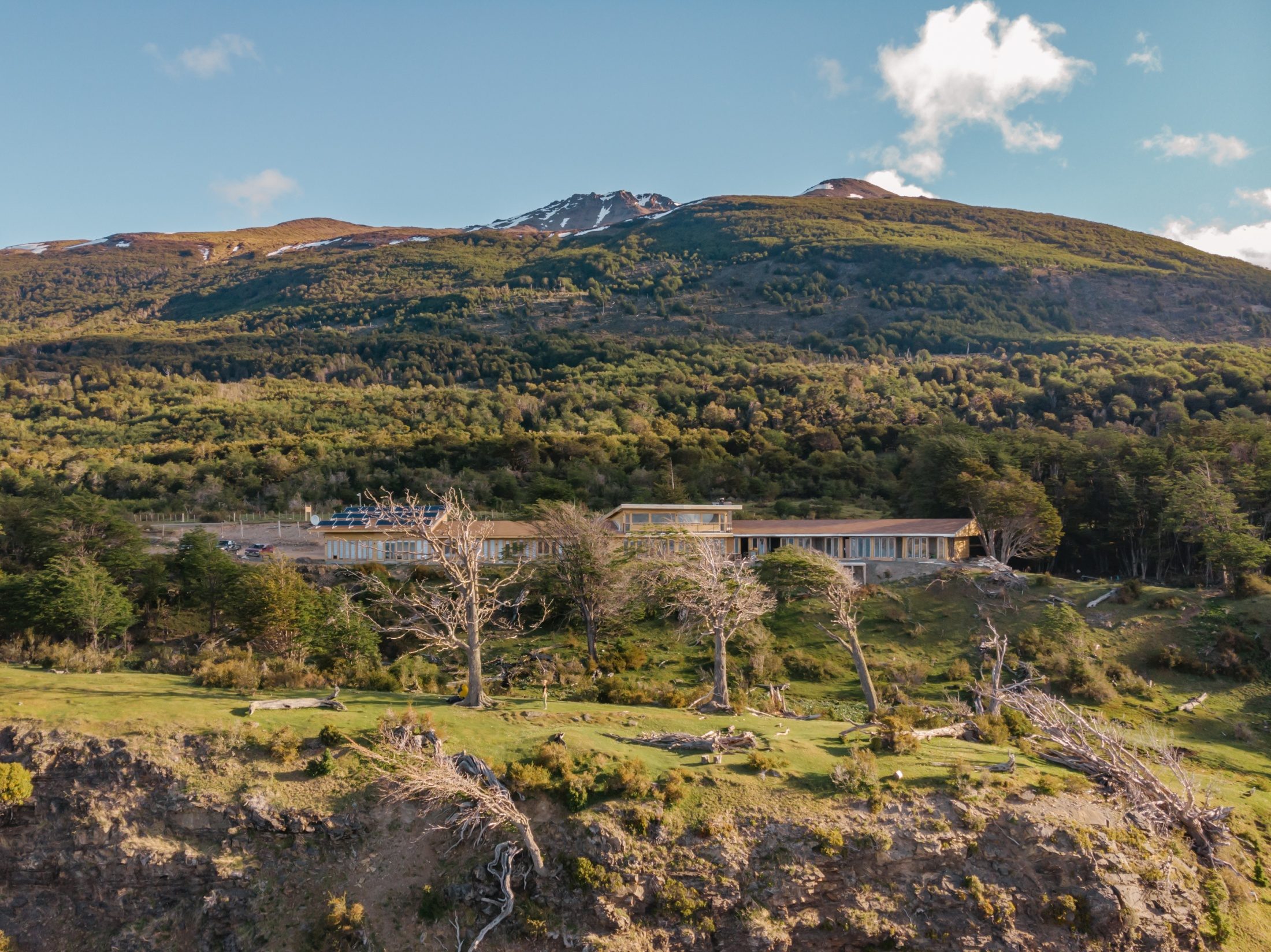 El lodge Errante en la ladera, entre el bosque de lenga y la costa, con el cerro detrás.