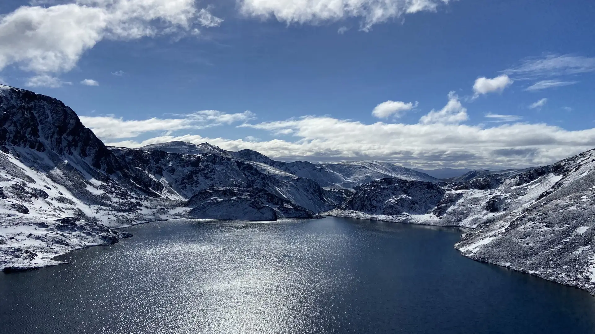 Lago de montaña rodeado de cerros nevados, bajo un cielo con nubes.