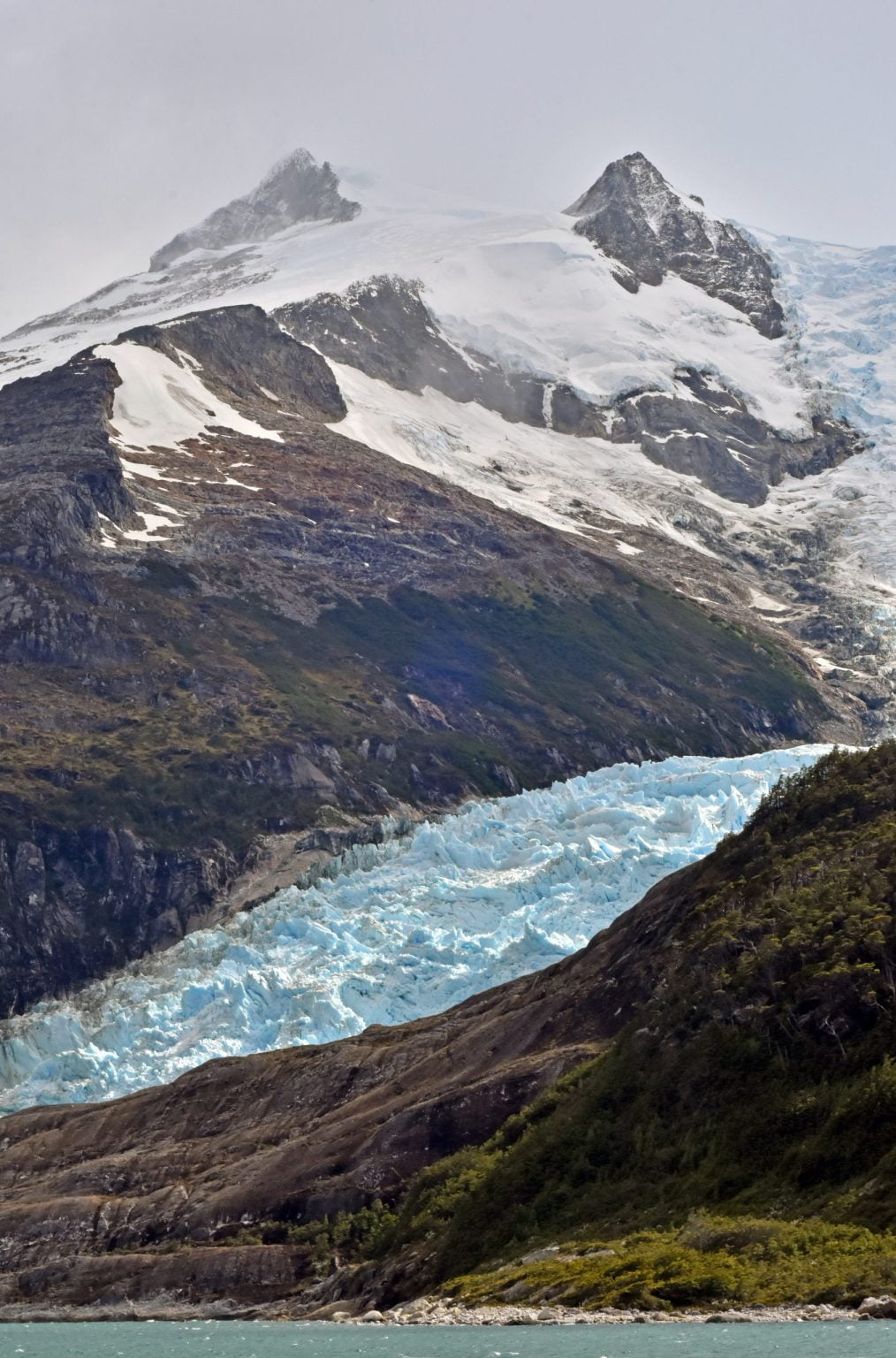 Glaciar entre cumbres nevadas que baja hasta el mar.