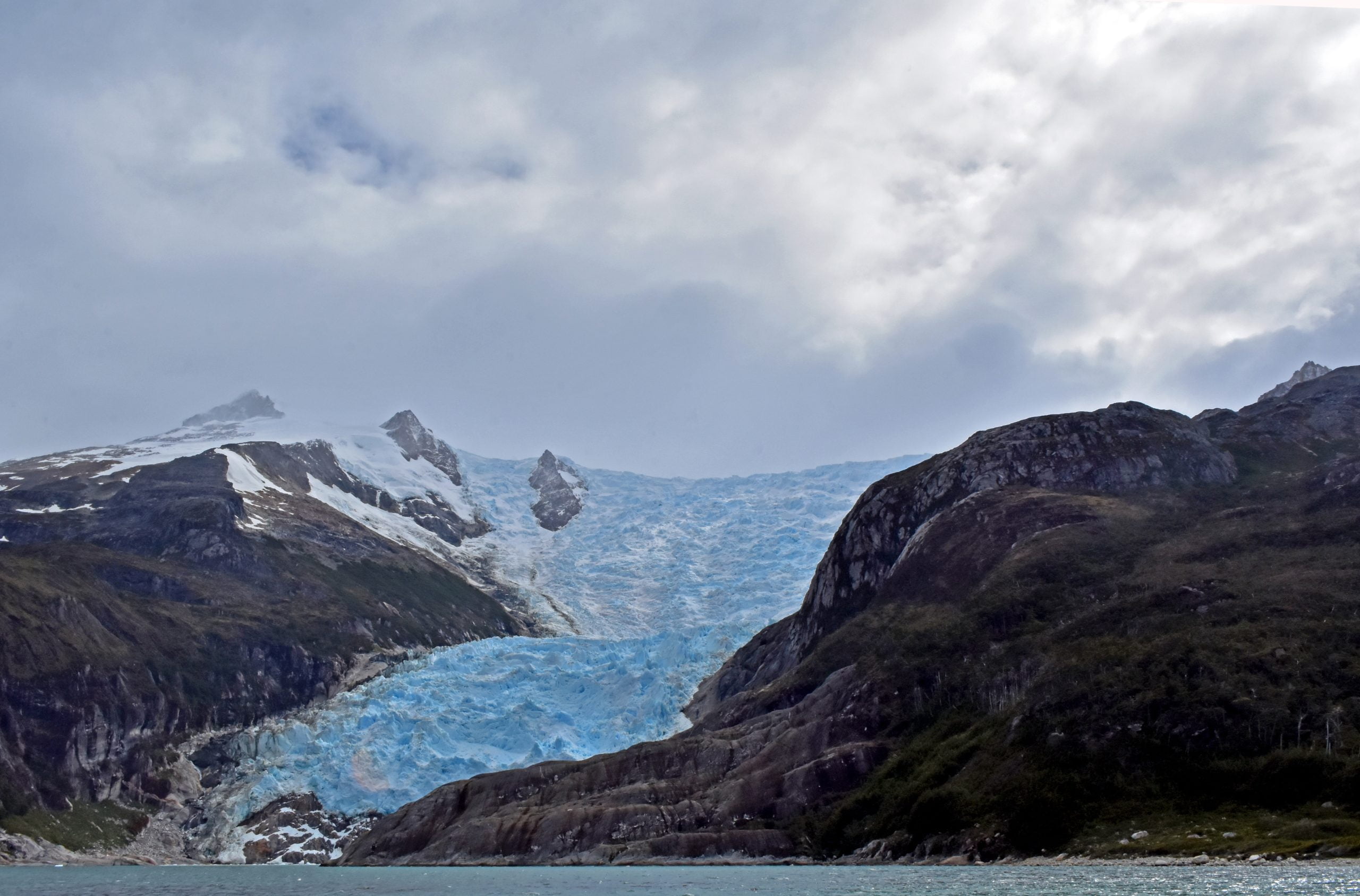 Glaciar que baja entre montañas hasta el agua.