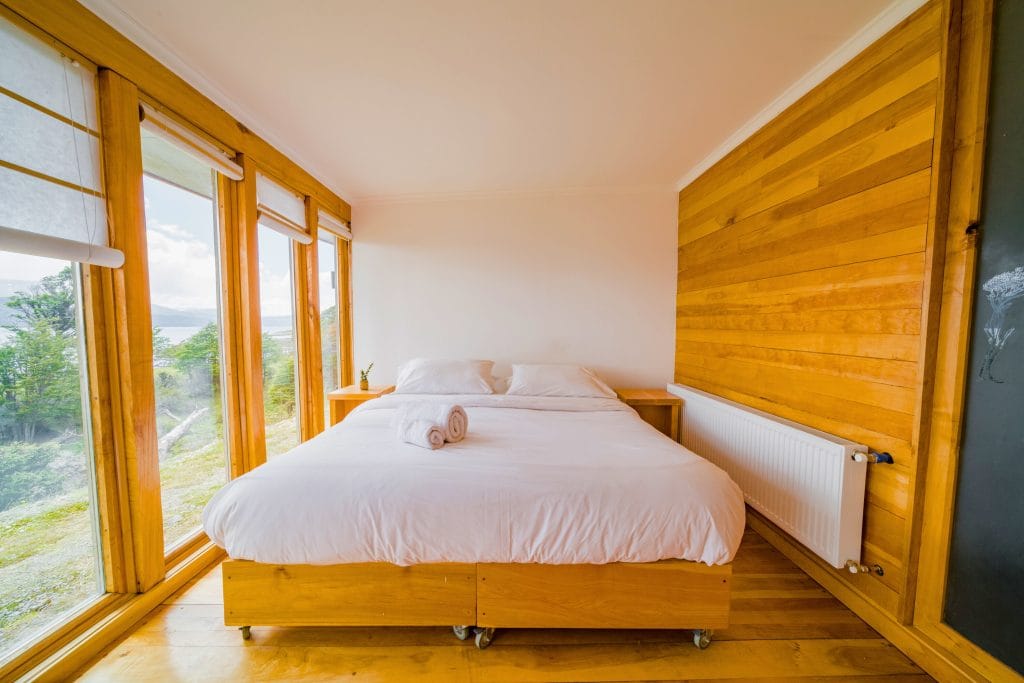 Habitación doble con cama grande, muro de madera de lenga y ventanal.