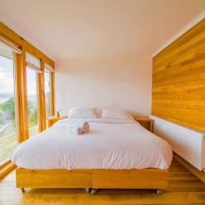 Habitación doble con cama grande, muro de madera de lenga y ventanal.