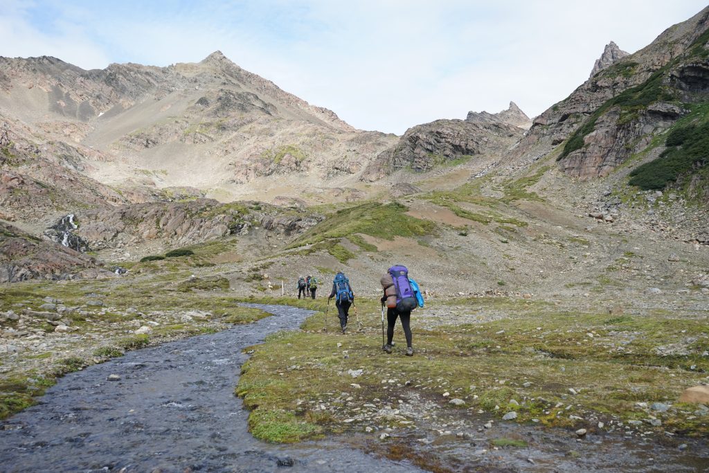 Caminantes con mochila avanzando por un valle de alta montaña.