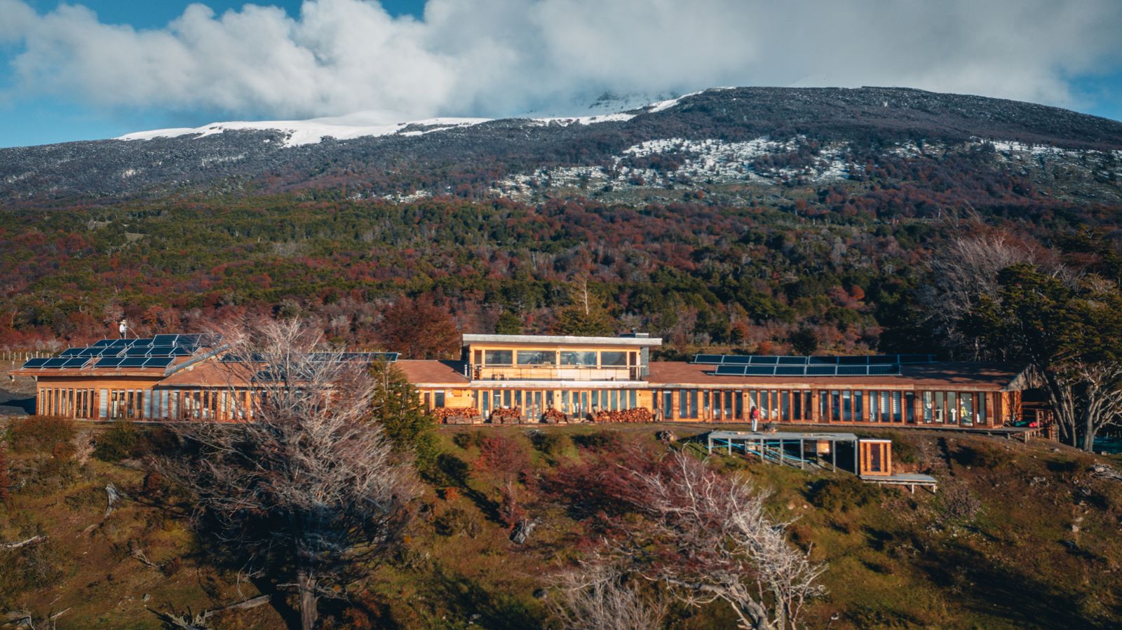 El lodge Errante en la ladera, entre arbustos de otoño y montañas con nieve.