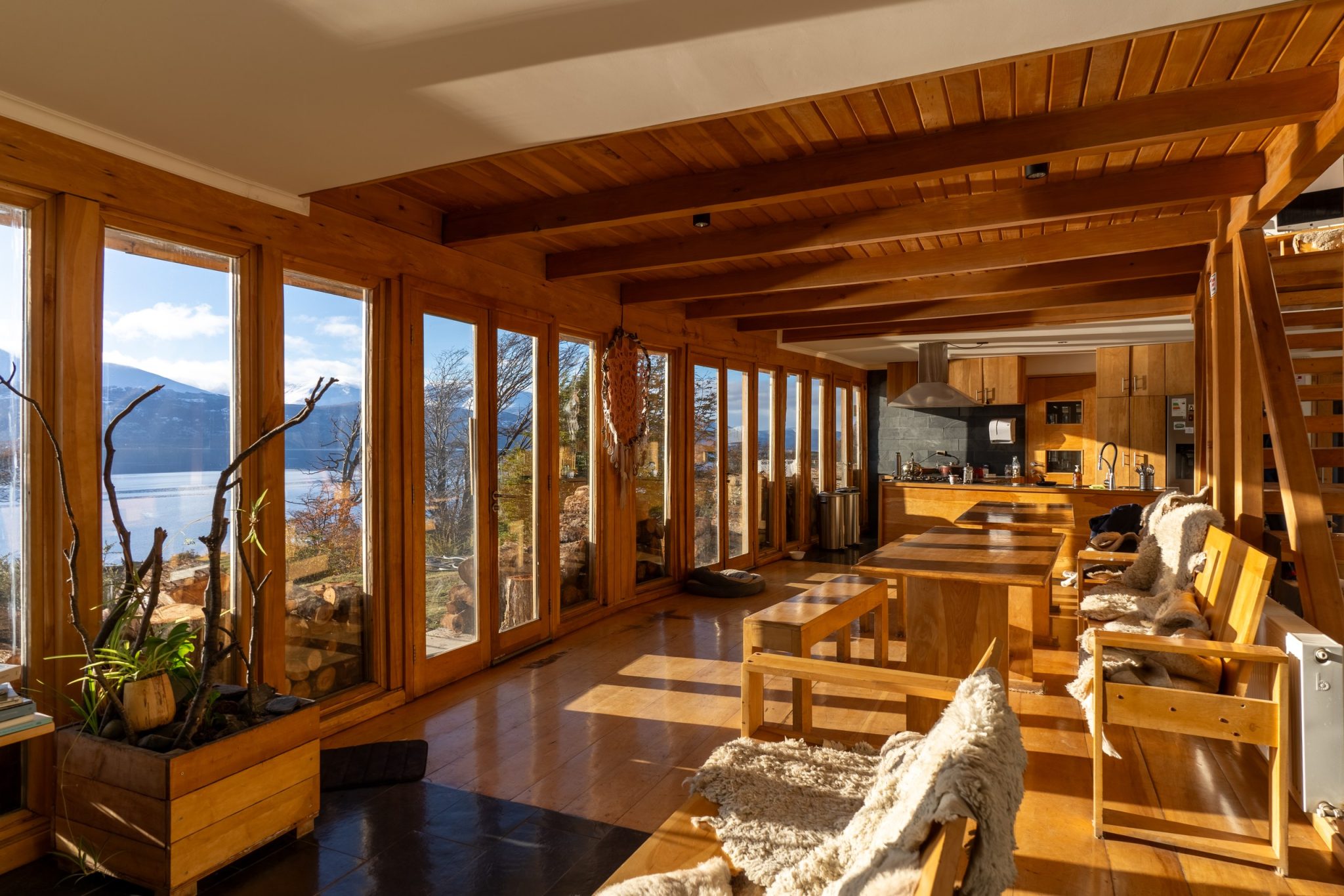 Comedor del lodge con mesas de madera y ventanales hacia el Canal Beagle, bajo el sol de la tarde.