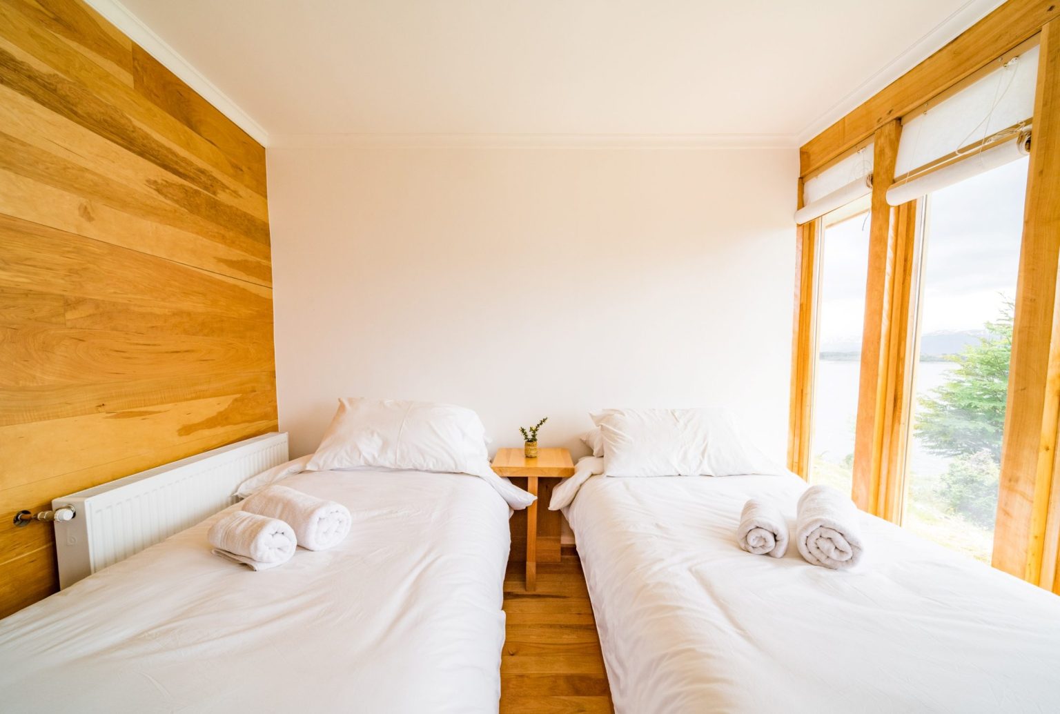 Habitación triple de Errante: dos camas junto a un muro de madera de lenga y ventanal al canal.