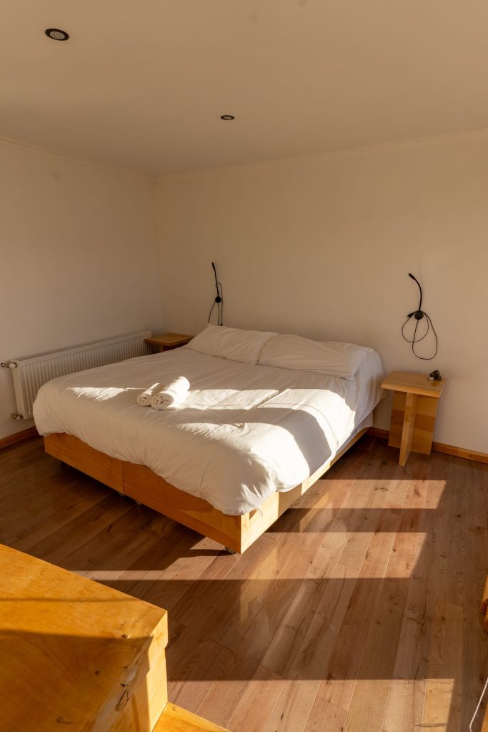 Habitación doble con cama grande y piso de madera, con luz de la tarde.