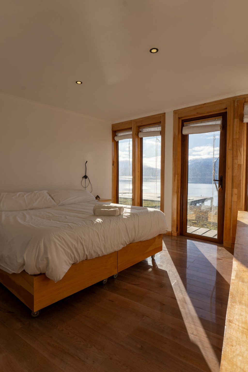 Habitación doble con cama grande, ventanal y puerta hacia la bahía y el Canal Beagle.