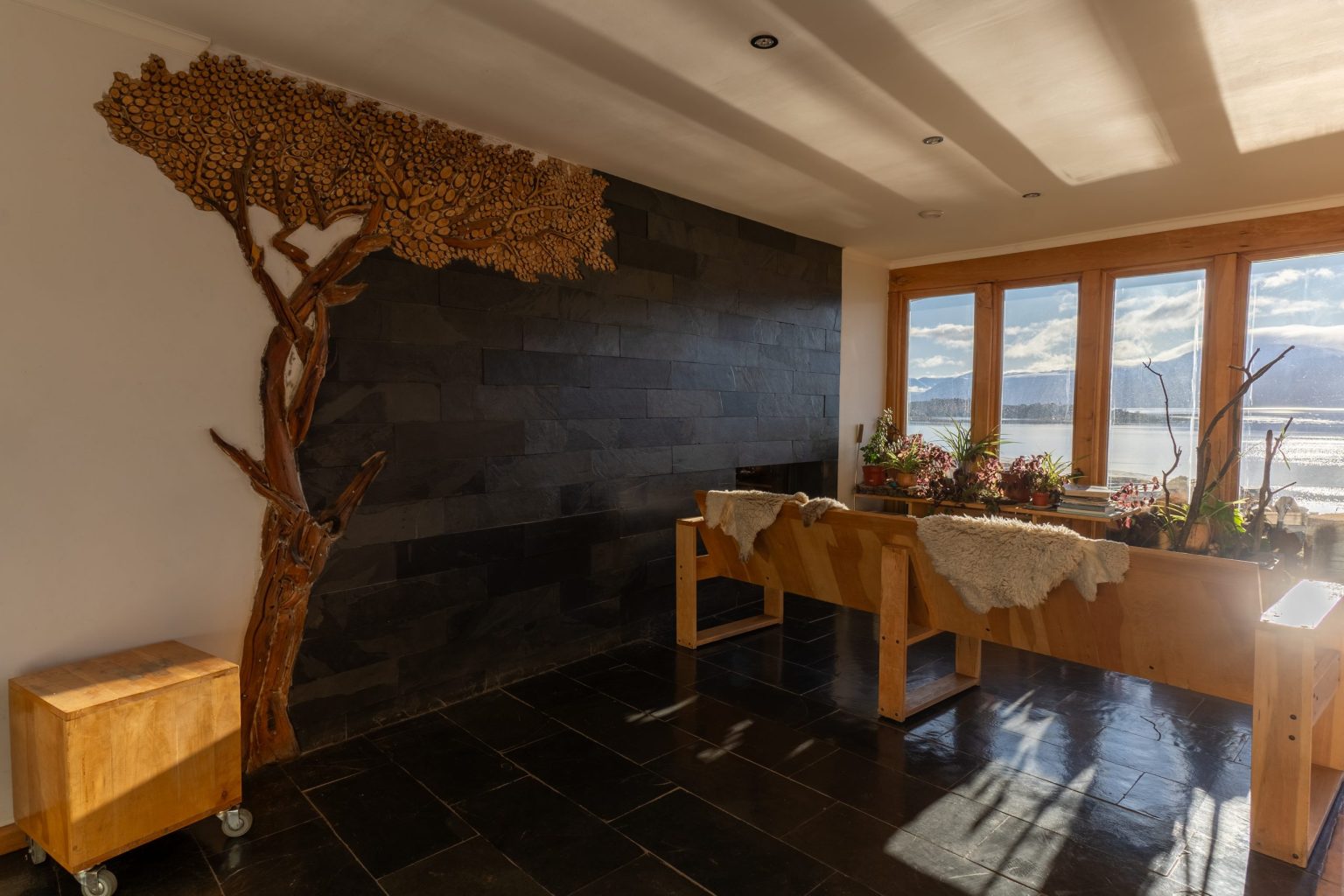 Living de Errante con la escultura de árbol en madera y ventanales hacia la bahía.