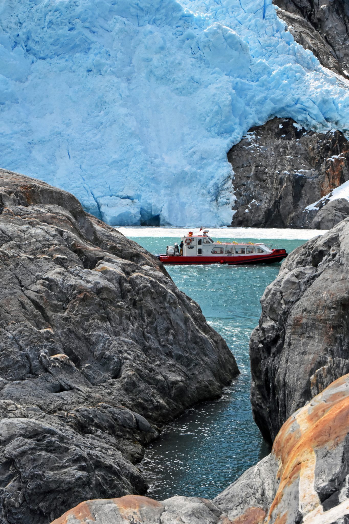 La embarcación LOICA enmarcada entre dos rocas, frente a la pared de hielo del glaciar.