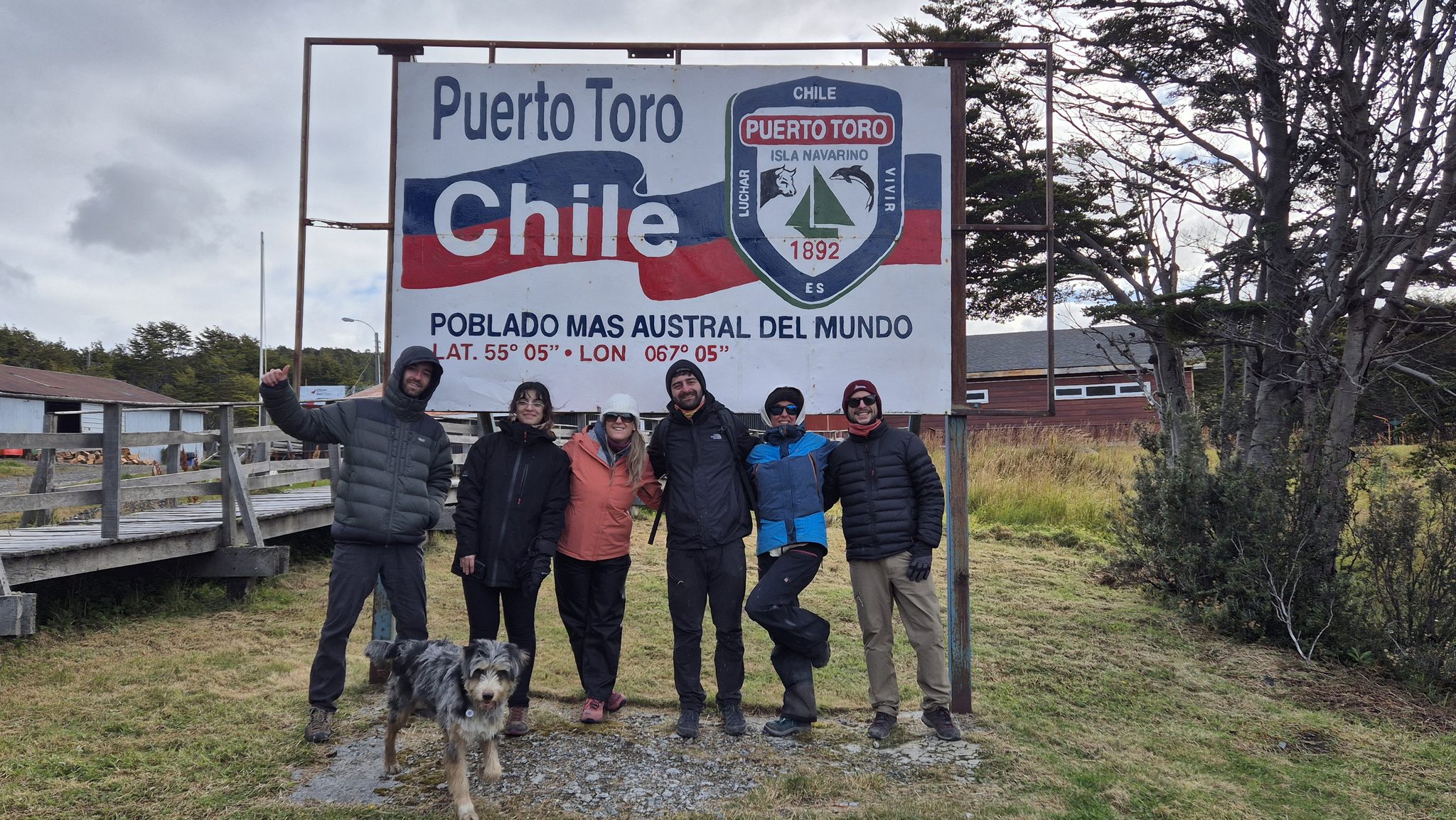 Un grupo de viajeros posa frente al cartel «Puerto Toro, Chile. Poblado más austral del mundo».