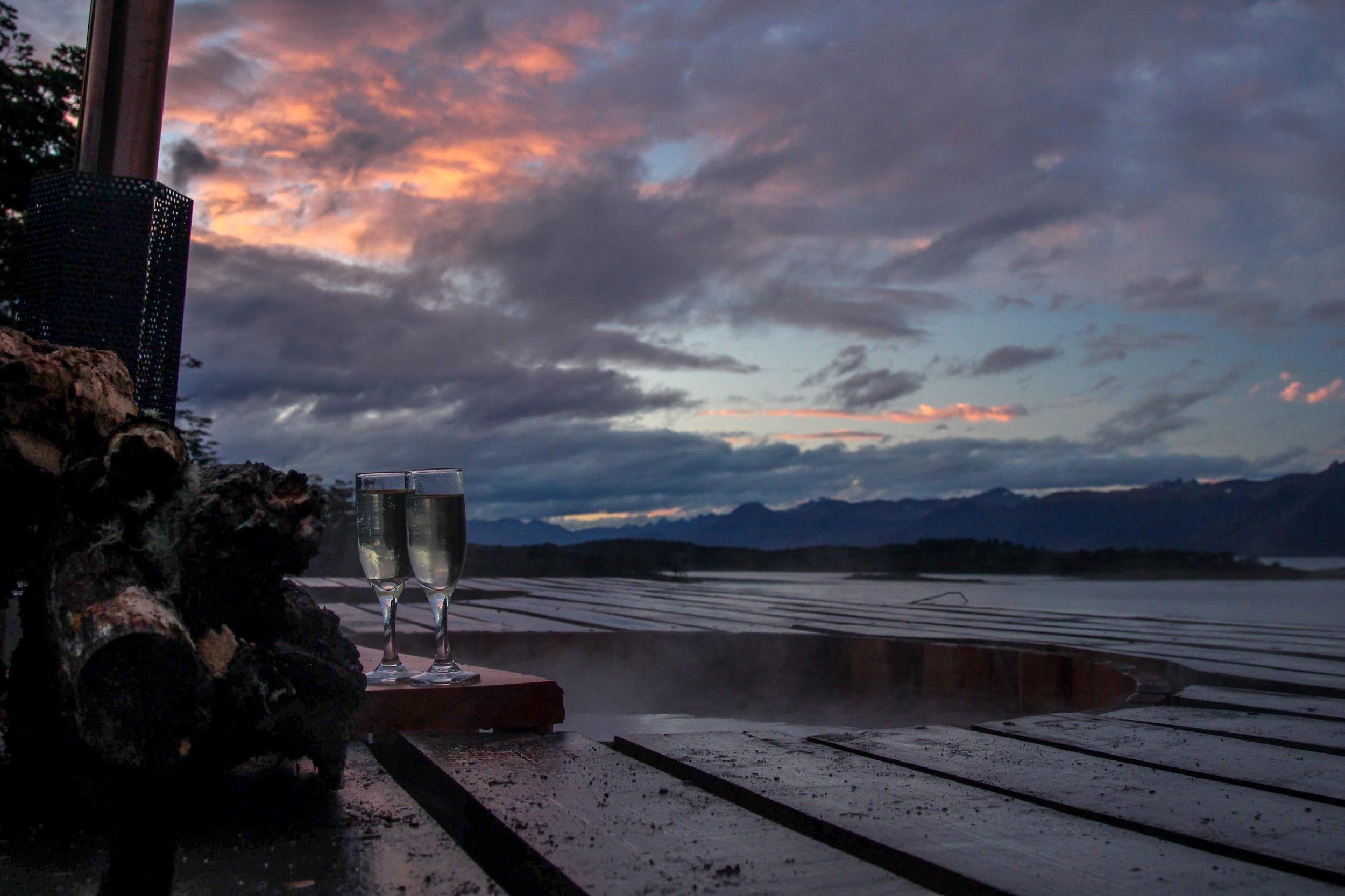 Tinaja caliente humeando en la terraza de Errante al atardecer, con dos copas y el canal al fondo.